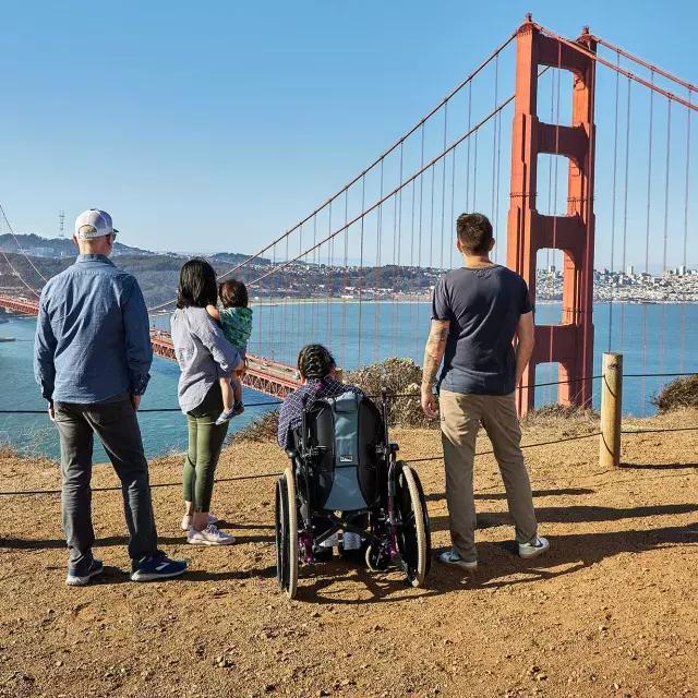 一群人, including one person in a wheelchair, is seen from behind as they look at the Golden Gate Bridge from the Marin Headlands.